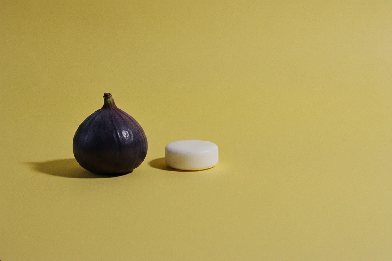 A whole purple fig and a small white disc resting separately on a bright mustard-yellow surface under harsh flash lighting