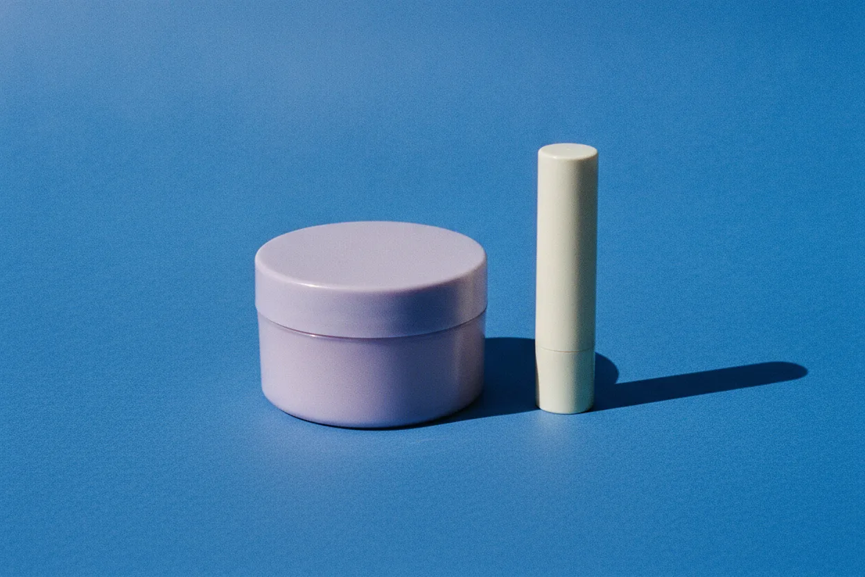 A lavender lip mask pot and a cream balm stick standing side by side on a bright cobalt blue background