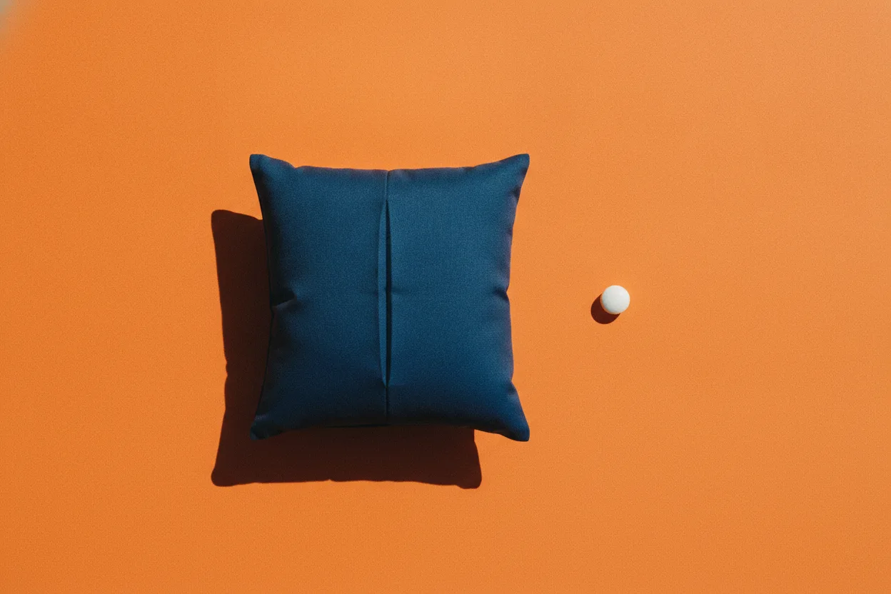 A navy-blue pillow and a single white pill sit apart on a bright orange surface under harsh flash lighting