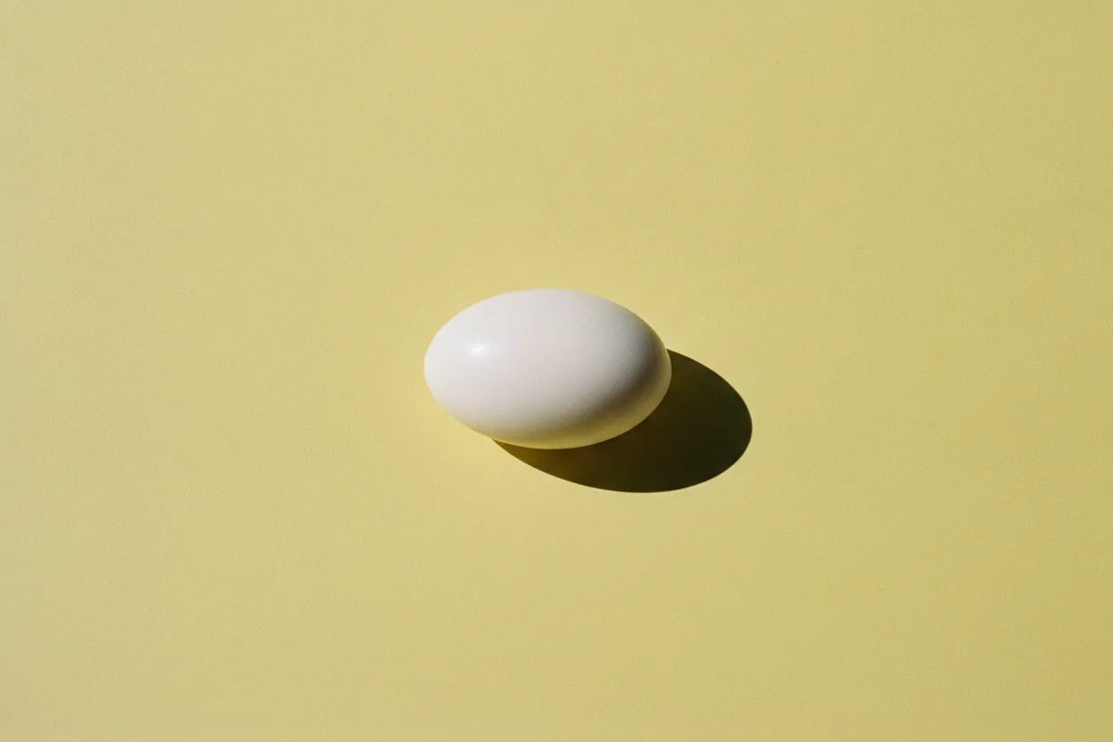 A smooth white oval bar of soap on a plain butter-yellow background, lit by hard flash with a crisp shadow